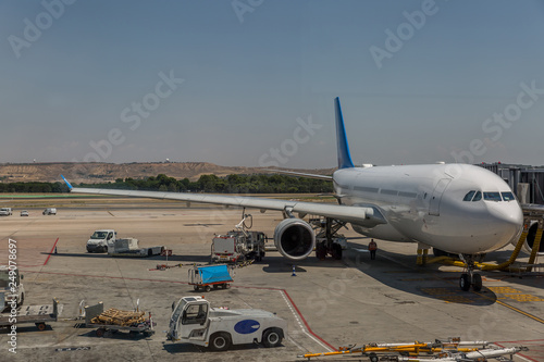 Commercial airplane parked on a runway preparing to fly, next to luggage transport vans and other vehicles
