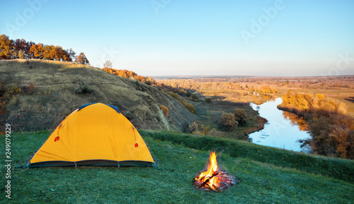 Orange tourist tent in green grass of hill above river