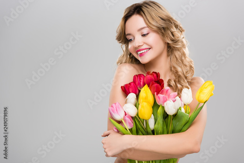 young beautiful smiling naked spring woman with bouquet of colorful tulips isolated on grey