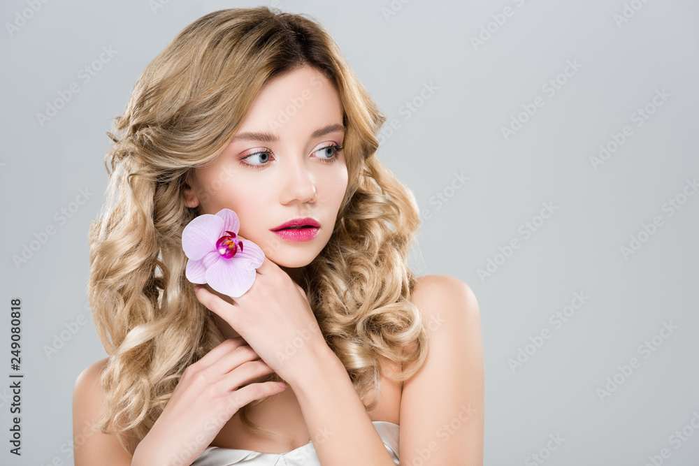 young beautiful woman holding purple orchid on hand and looking away isolated on grey - obrazy, fototapety, plakaty 