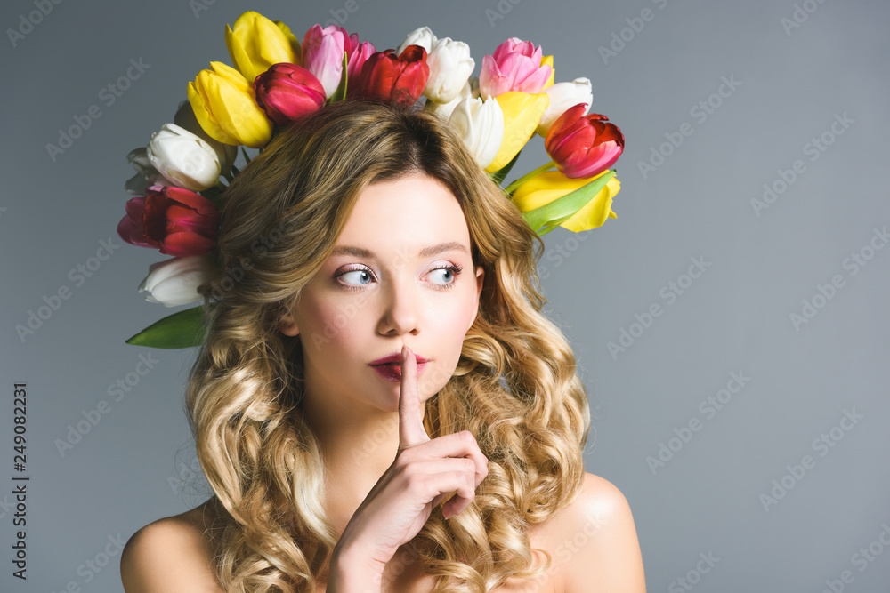 girl with wreath of flowers on hair showing hush sign isolated on grey