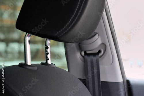 Black car headrest with selective focus and metal protect element. Blurred automobile safe passenger seat belt on background. Comfortable car headrests with shiny chrome height adjustment 