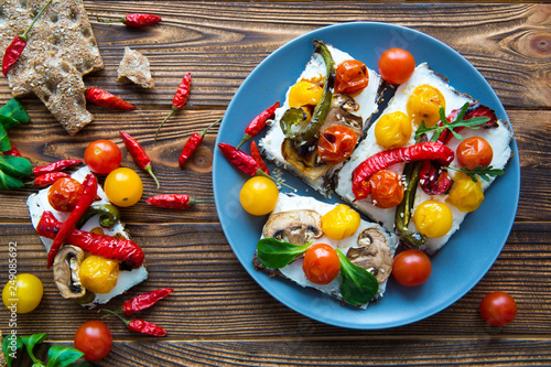 Plate of tasty appetizer with grilled paprik and tomatoes and creamy cheese on decorated wooden table. Little paprika decorations. Top view.  photo