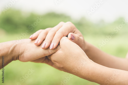 close-up of a daughter holding her mother's hand outdoors over nature background  © doucefleur