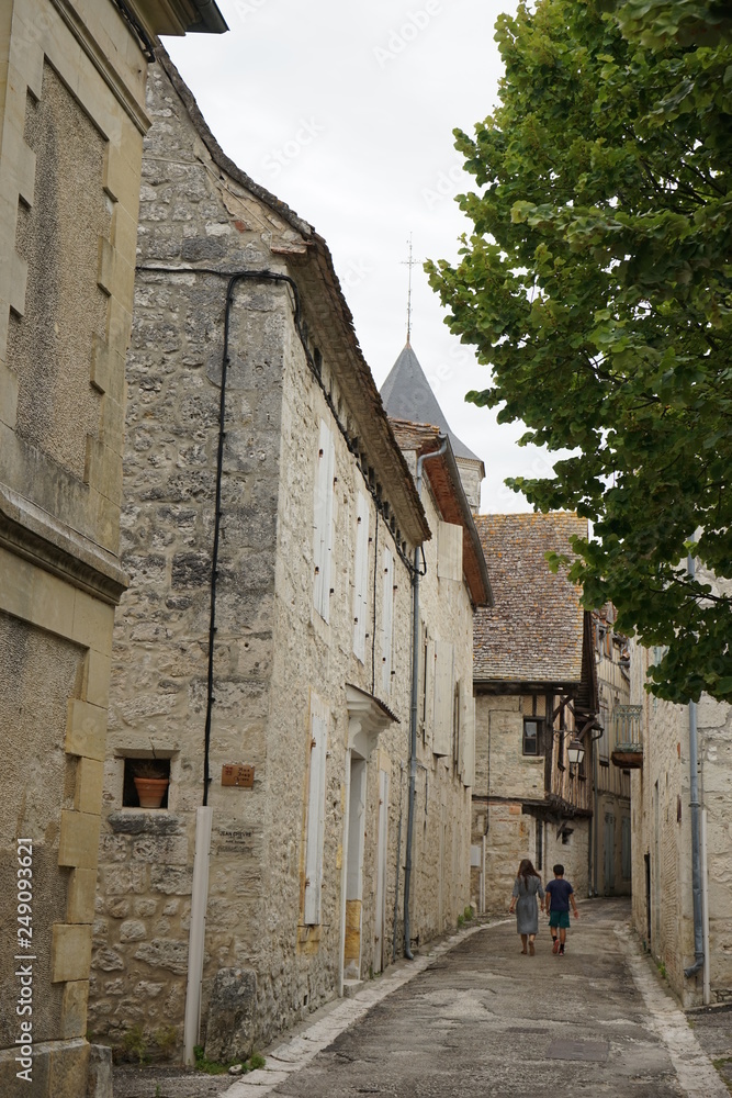 Narrow street in old town in France, stone houses, two people just visible walking away, Issigeac, France