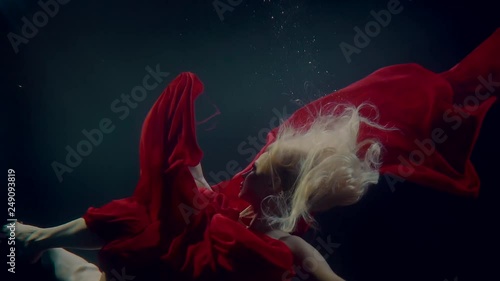 Blonde woman is sinking in dark water of lake, subaquatic view