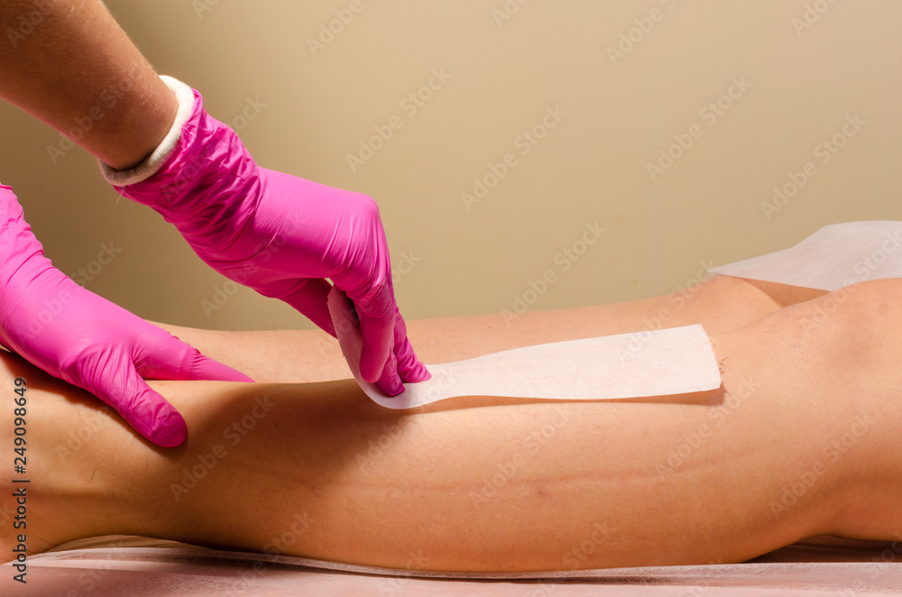 Fototapeta premium Beautician waxing a woman's leg applying a strip of material over the hot wax to remove the hairs when pulled