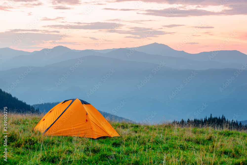 Orange tent on meadow in mountains under pink sky