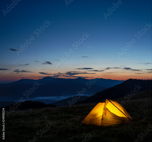 Orange lighted tent in mountains under evening sky