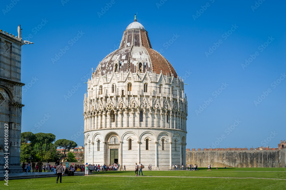 Pisa Baptistery beautiful decorated historic tower and tourists walking at the central square of Pisa. Tuscany, Italy.