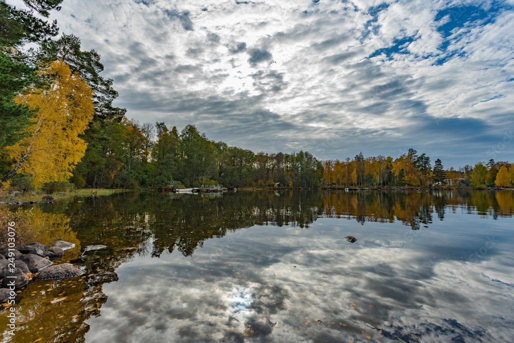 Picture of beautiful autumn lake with yellow and green trees and reflection of blue cloudy sky on the water