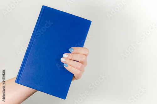 Closeup view of one beautiful female hand holding blue paper book with empty cover. Horizontal color photography.