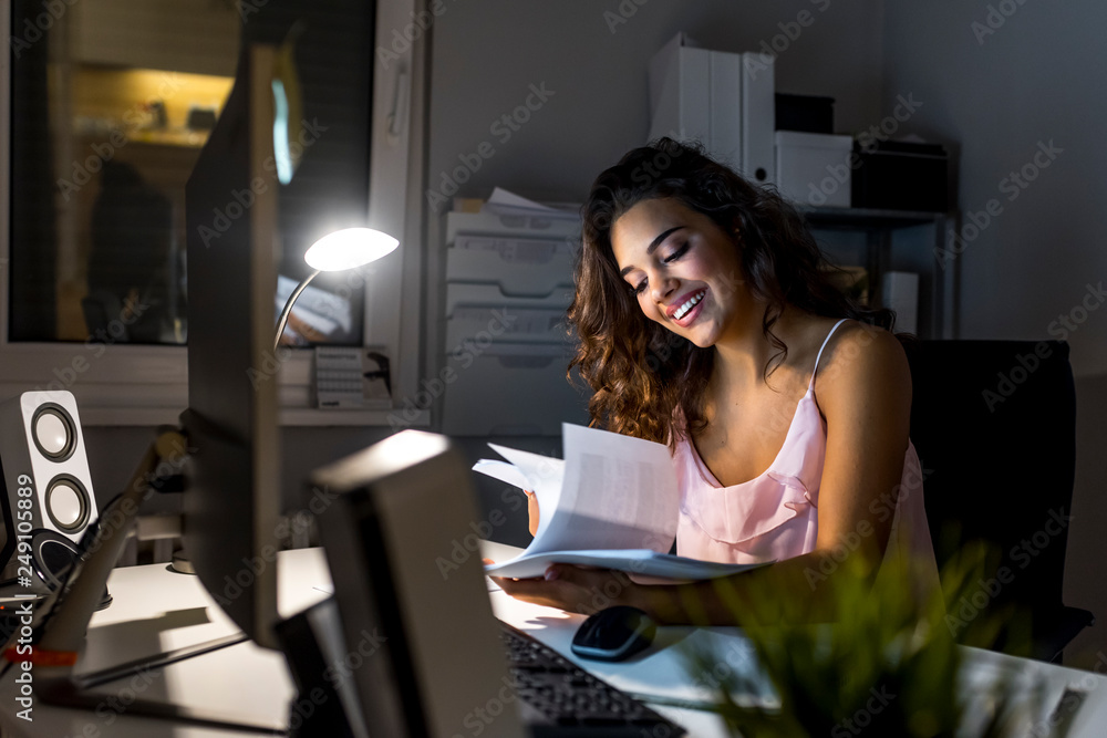 Happy young woman sitting in office and working