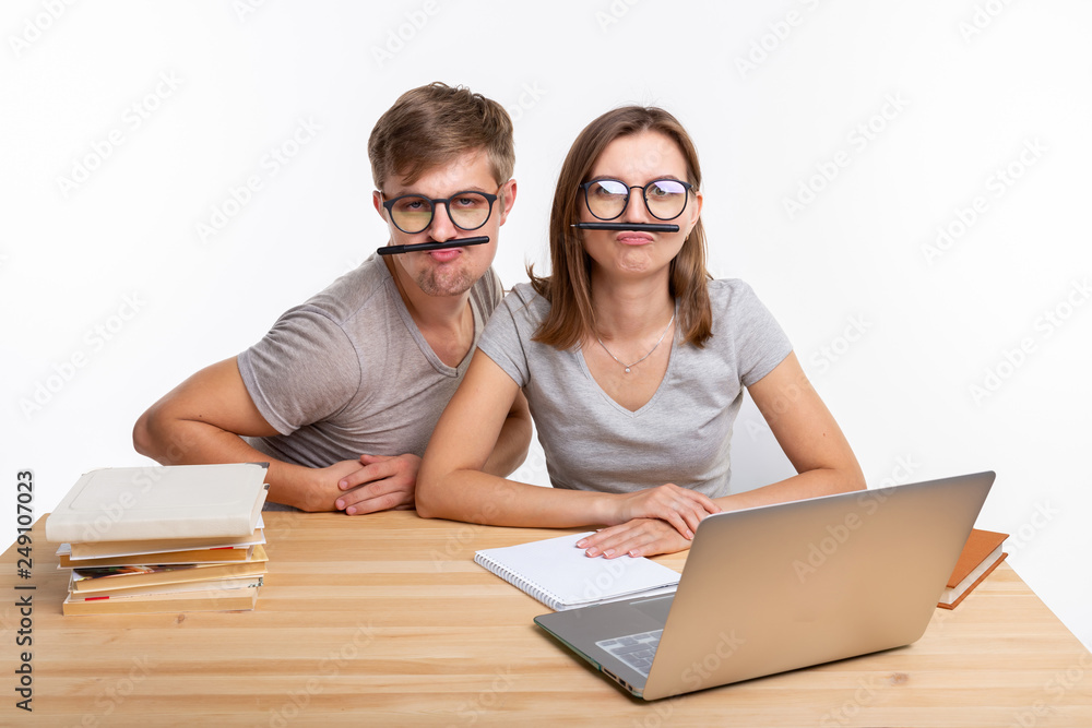 Education and people concept - a couple of young students in glasses look like they are bored of learning homework and make a stupid jokes Education and people concept - a couple of young students in glasses look like they are bored of learning homework and make a stupid jokes