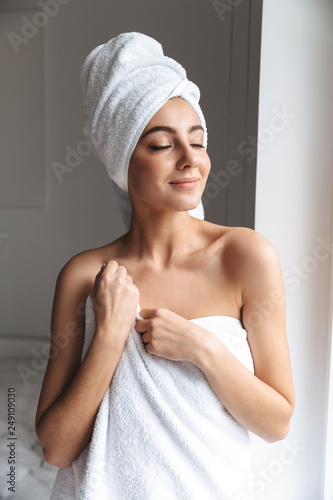 Photo of pretty woman wrapped in white towel, standing in room after shower