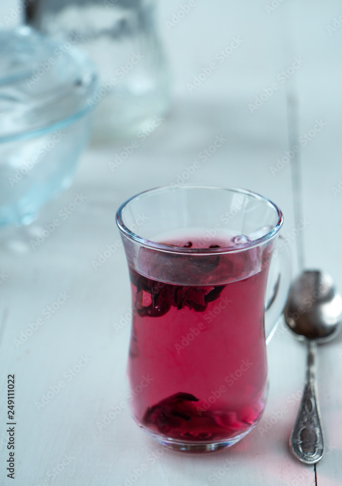 Red carcade tea in transparent glass cup at white wooden background, simple and nice drink picture for calm and peaceful rest time illustration. Red carcade tea in transparent glass cup at white wooden background, simple and nice drink picture for calm and peaceful rest time illustration.