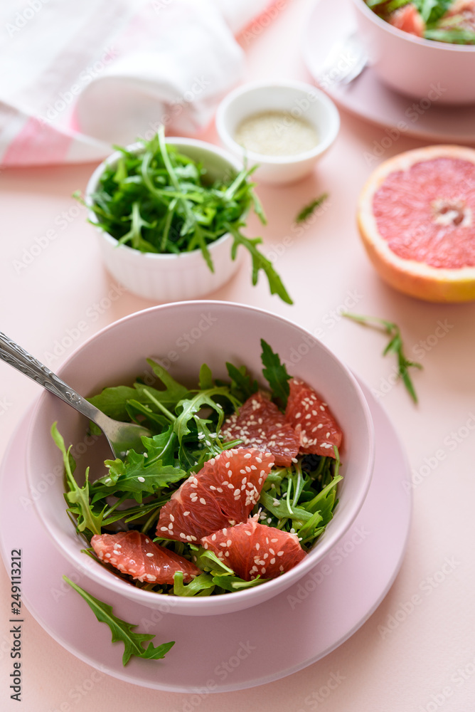 Fresh citrus salad with arugula, grapefruit and sesame seeds on pink background. Selective  focus. Raw vegetarian spring detox food
