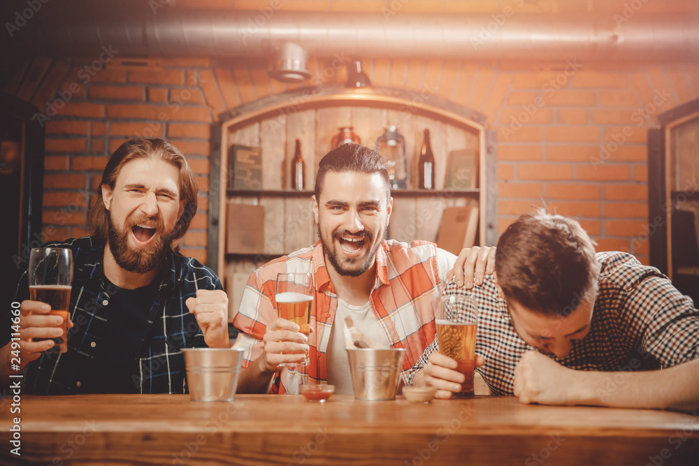 Men watch game on TV screen in pub, drinking beer, shouting and cheering for players