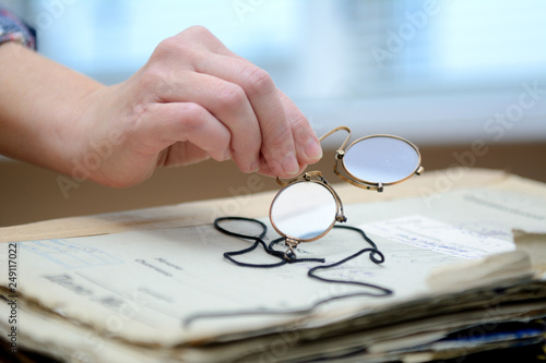 female fingers hold pince-nez over old papers