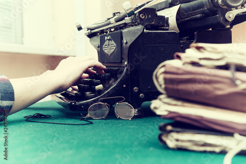 above the keys of an old typewriter female fingers. On the green cloth of the table pince-nez and folders