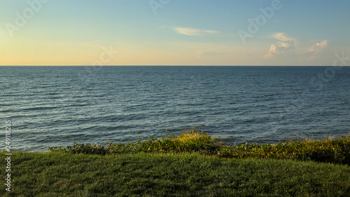 A beautiful view of the lake Ontario with a green lawn in the base, the lake in the middle and the sky on the very top of the picture