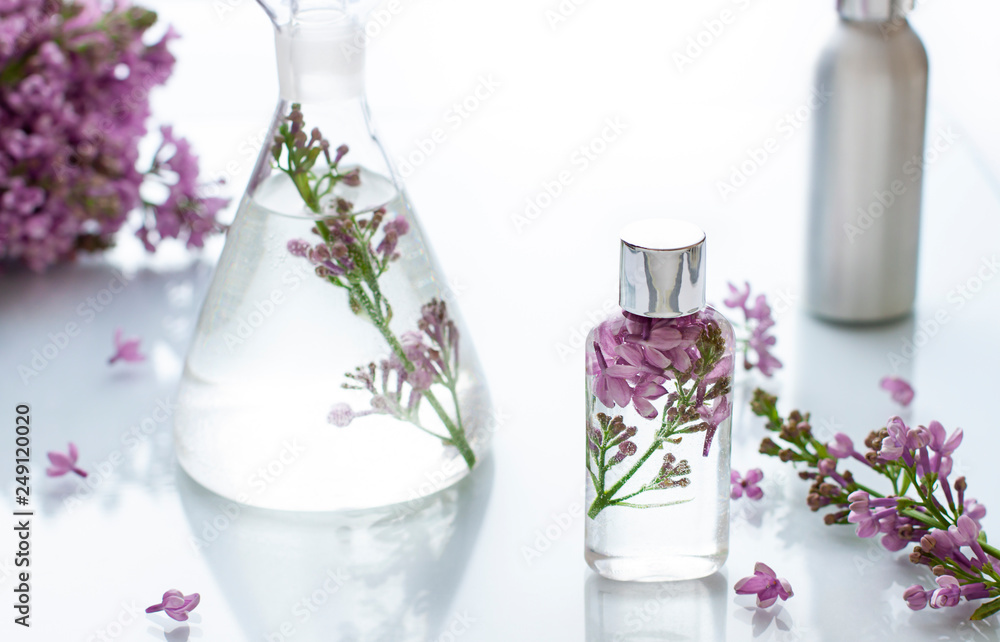 Cosmetic bottle close up with lilac flowers on the white background