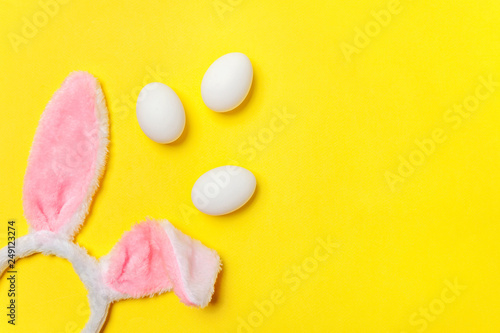 Happy Easter concept. Preparation for holiday. Decorative white eggs and bunny ears furry costume toy isolated on trendy yellow background. Simple minimalism flat lay top view copy space