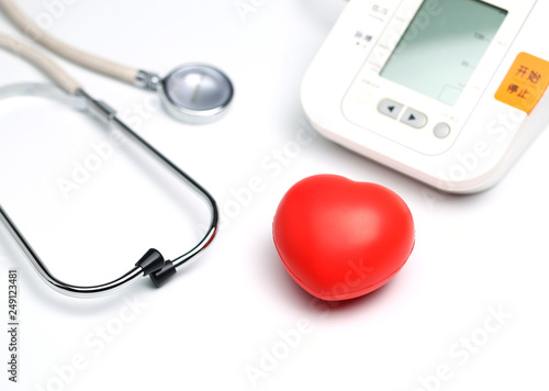 Sphygmomanometer, red heart and stethoscope on white table, close up view