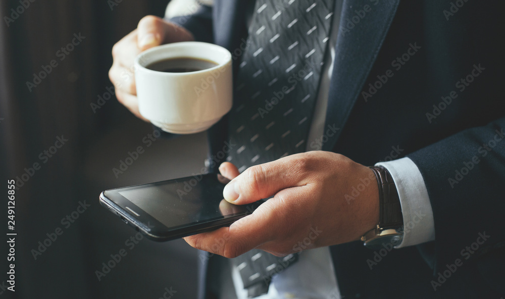 young businessman in dark office with smartphone tablet and coffee