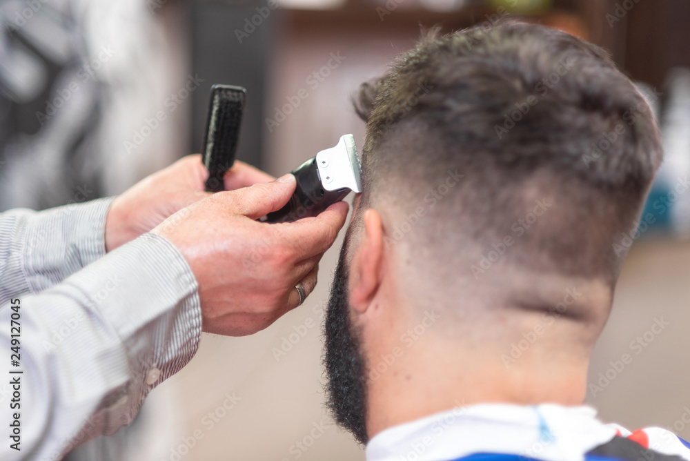 Handsome bearded man, getting haircut by barber, with electric trimmer at barbershop . Handsome bearded man, getting haircut by barber, with electric trimmer at barbershop .