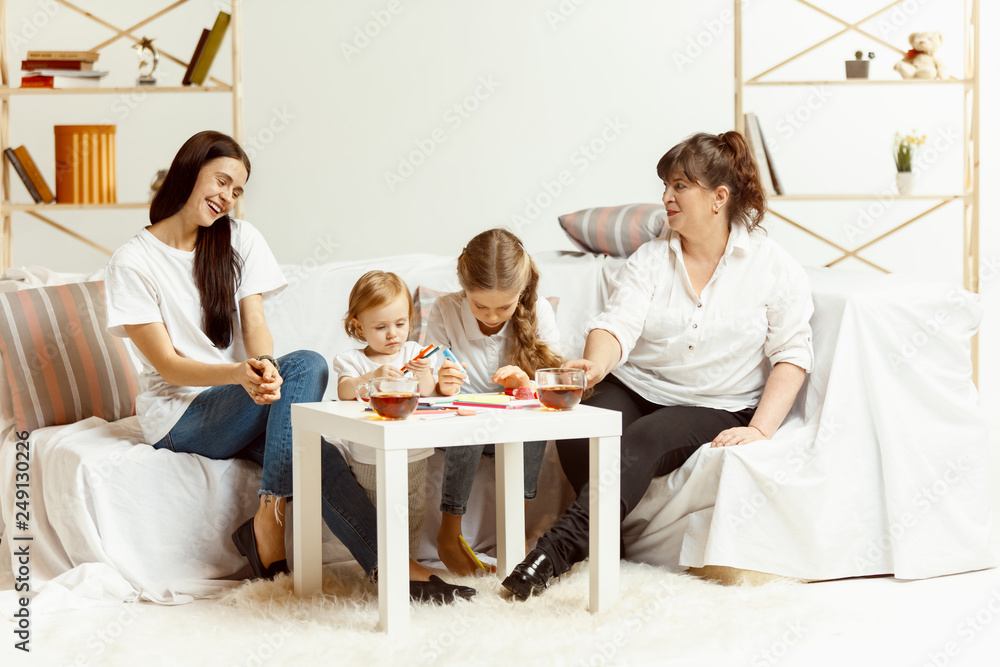Φωτογραφία Two little girls their attractive young mother and their charming grandmother sitting on sofa and spending time together at home