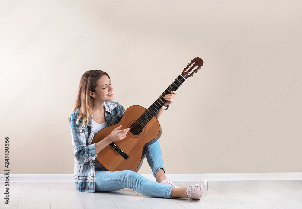 Young woman playing acoustic guitar near grey wall. Space for text