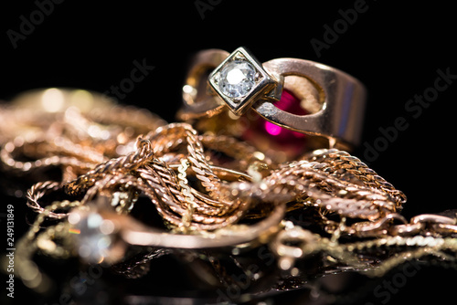 Real gold rings with diamonds, gold chains close up shot on shiny black background.