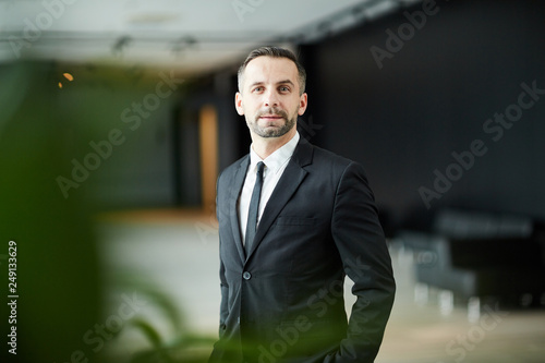 Young serious businessman in suit looking at you in contemporary airport lounge environment