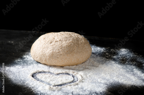 Heart painted on flour. Dough with spilled flour on a black background. Yeast dough for bread, rolls, pizza or pie.