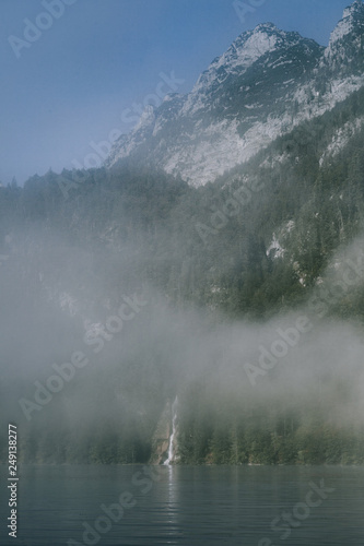 views of forest among fog in border of the lake with a waterfall