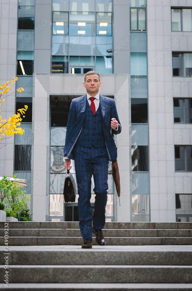 Serious businessman in a checkered stylish suit coming down the stairs. Business life in the city.