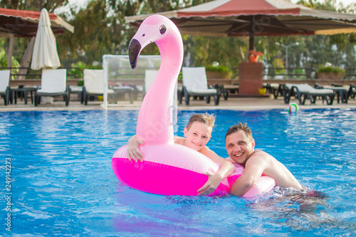 Happy young family having fun together at the swimming pool outdoors in summer, swimming with inflatable flamingo. Aquapark. © MartaKlos