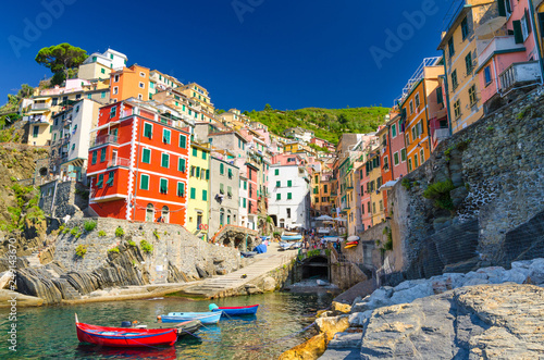 Riomaggiore traditional typical Italian fishing village in National park Cinque Terre with colorful multicolored buildings houses on hill and boats on water, clear blue sky background, Liguria, Italy