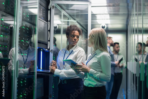Two women are working in a data center with rows of server racks photo
