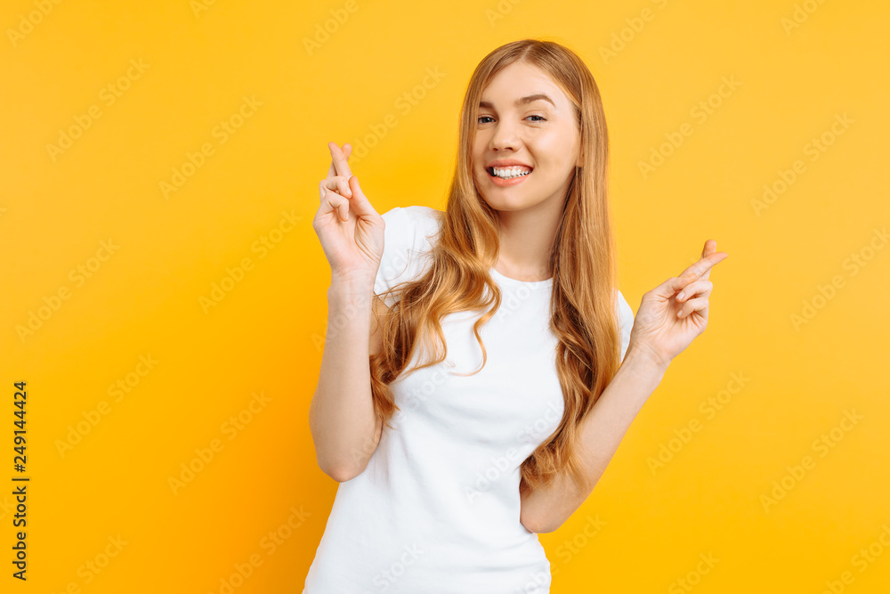 Portrait of a smiling pensive young girl standing on a yellow background, fingers crossed for luck Portrait of a smiling pensive young girl standing on a yellow background, fingers crossed for luck