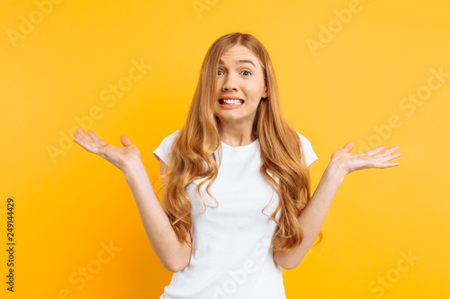 woman shrugs, with indecisive expression on her face, depicts misunderstanding and uncertainty on a yellow background