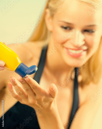 Young happy smiling beautiful tanned woman applying sun protection cream on sea beach