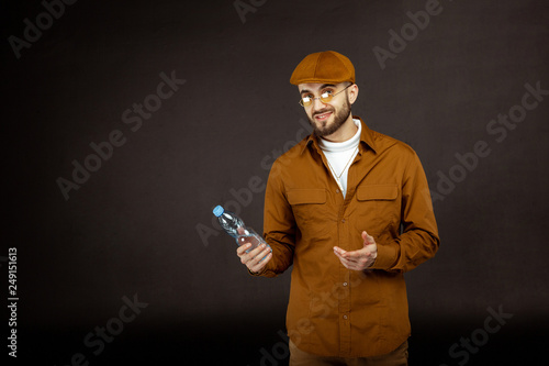 Young bearded man, model in beige shirt and yellowe sunglusses holding bottle in hand photo