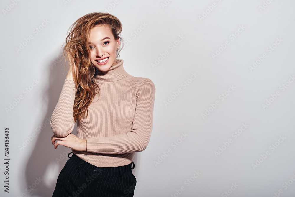 Shine bright. Young girl with charming smile posing in studio, touching her hair and looking at camera isolated over white background Shine bright. Young girl with charming smile posing in studio, touching her hair and looking at camera isolated over white background