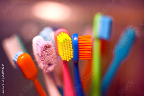 Bright multi-colored toothbrushes standing in a glass with a blurred background.