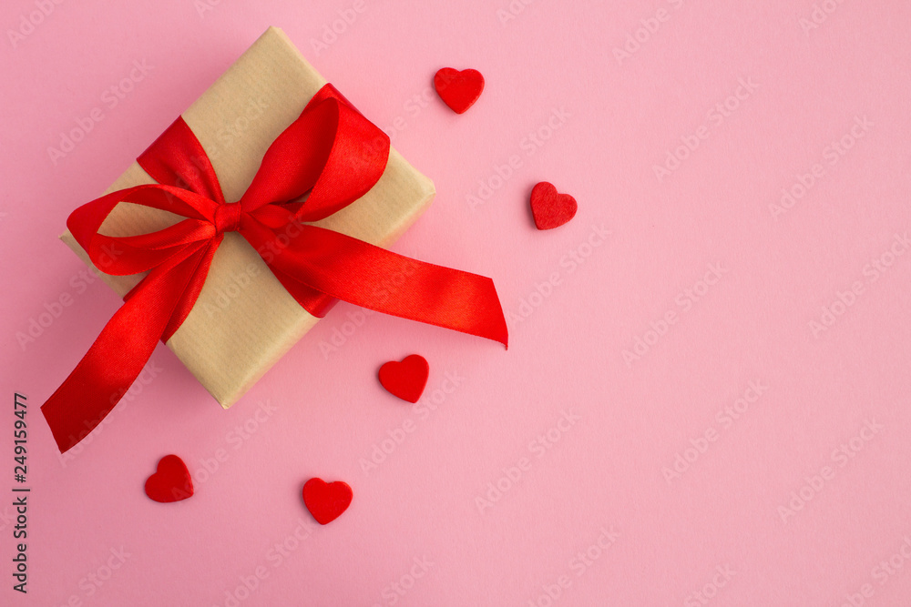 Gift with red bow and small red hearts on the pink background.Top view.Copy space. Gift with red bow and small red hearts on the pink background.Top view.Copy space.