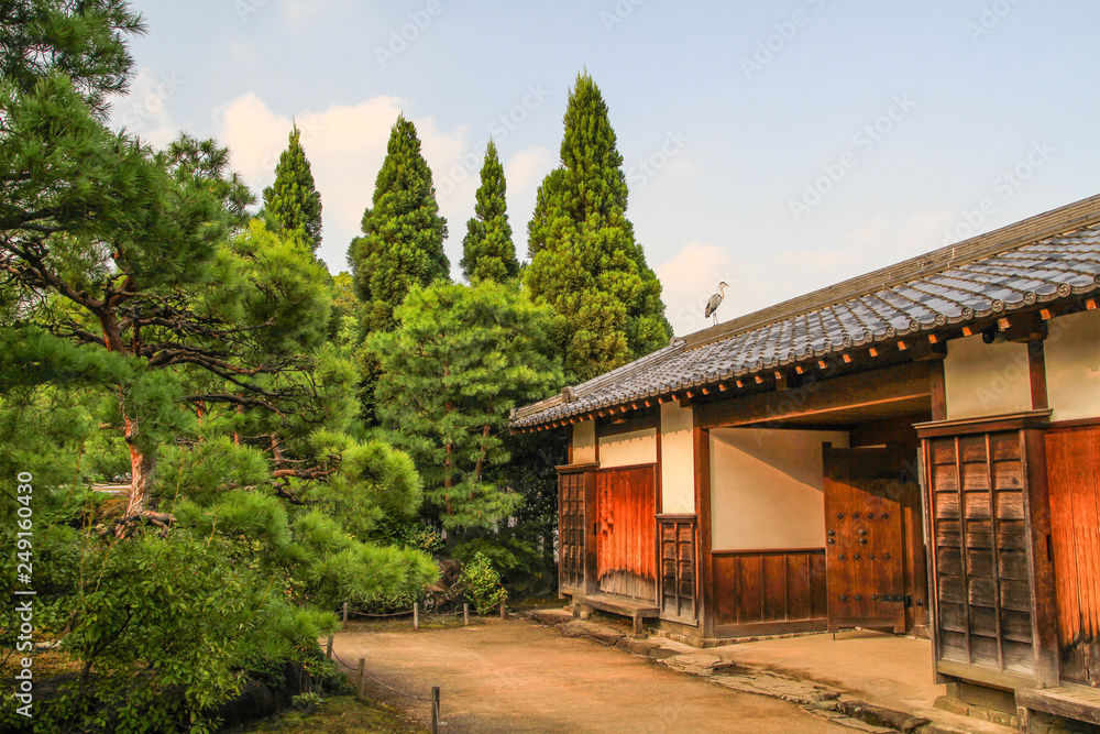 Graureiher auf dem Dach eines traditionellen japanischen Hauses umgeben von Kiefern, aufgenommen in einem japanischen Garten in Himeji, Japan