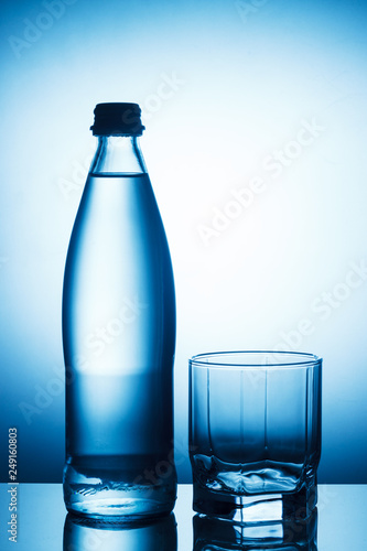 Bottle of water and empty glass on blue background