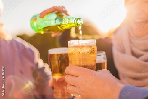 Group of happy friends drinking beer and having fun - young smiling girl pouring beer from green bottle